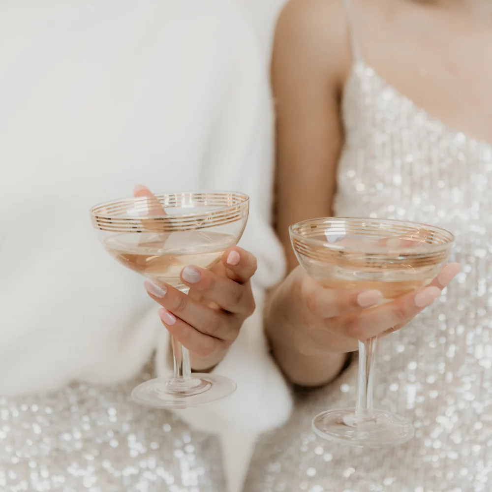 Women in sparkly dresses holding coupe glasses of pink champagne